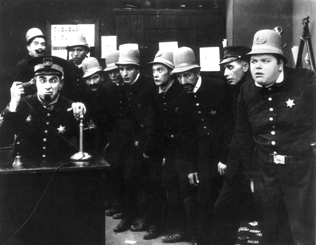 A scene from 'In the Clutches of the Gang', a Keystone Cops silent comedy directed by George Nichols and Mack Sennett. Left to right : Ford Sterling (on phone), Edgar Kennedy, George Jeskey, Al St John, Hank Mann, Rube Miller, and Roscoe Fatty Arbuckle (1887 - 1933).   (Photo by Hulton Archive/Getty Images)